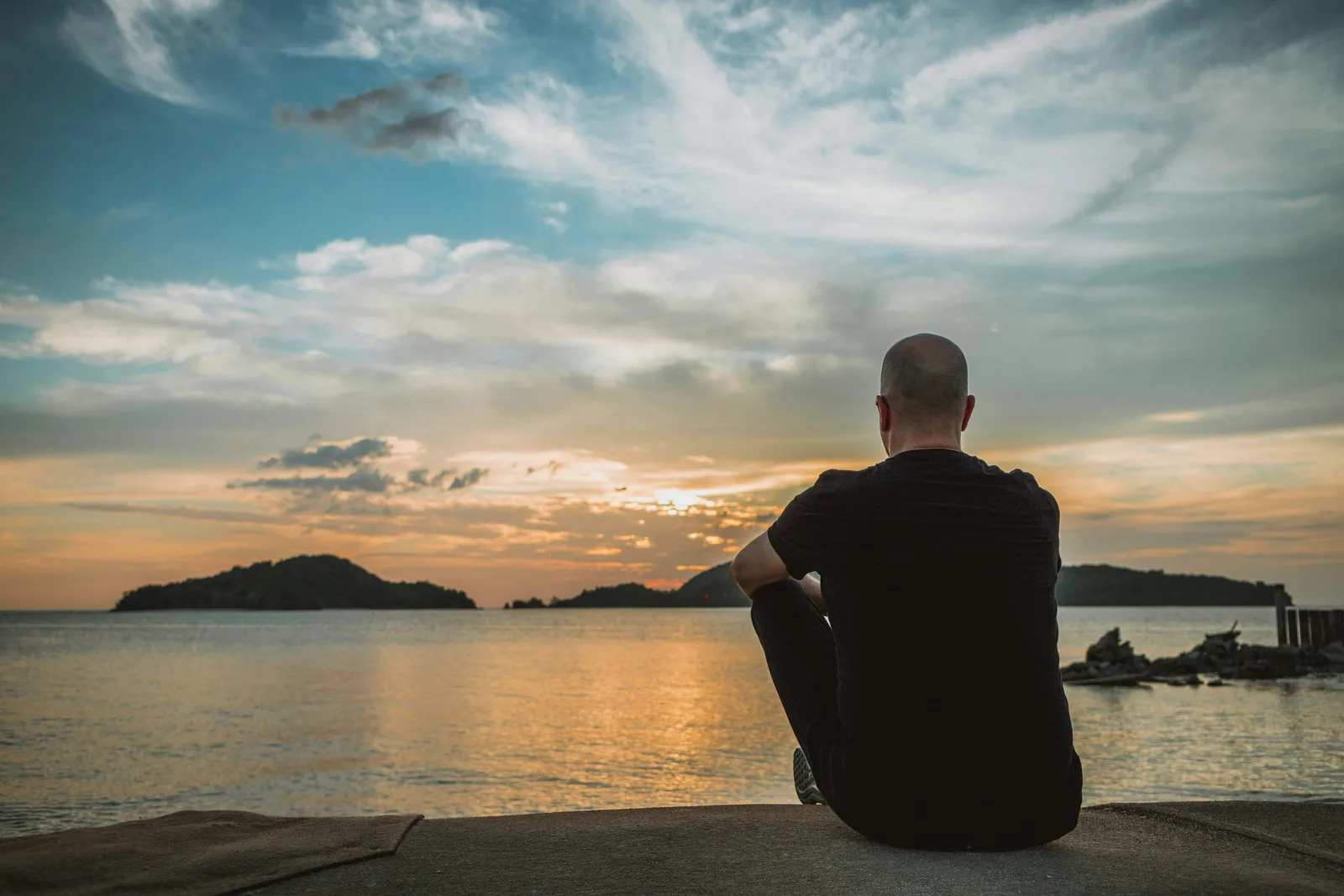 A person sitting alone looking out over water at dusk